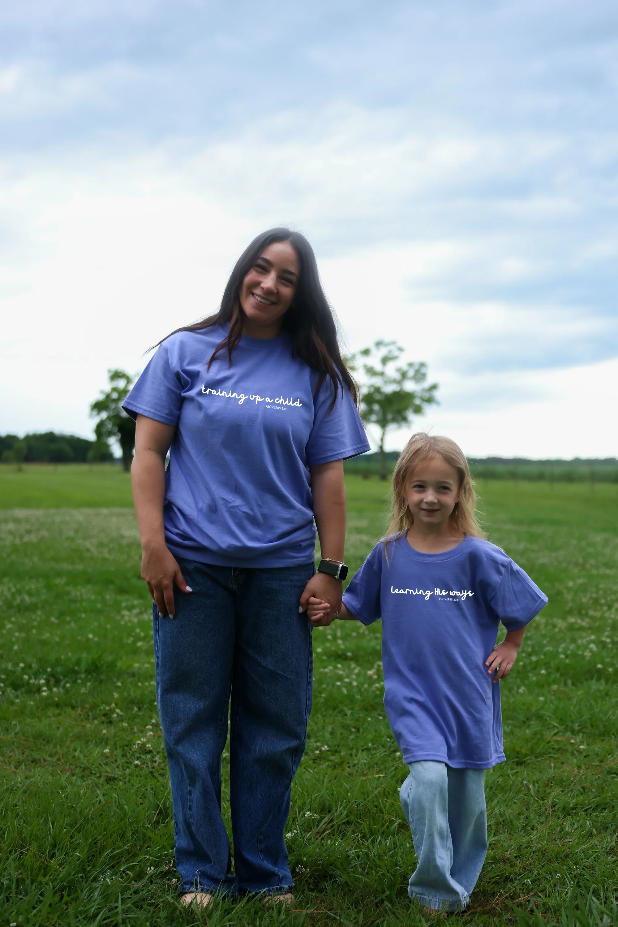 A mother and daughter wearing matching faith-inspired tees in an open field