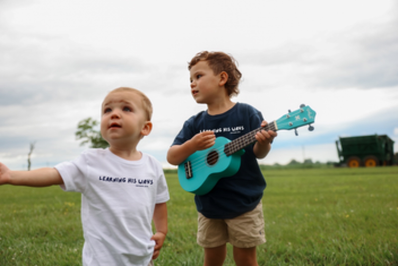 Two children wearing Learning His Ways tees and playing with a ukulele